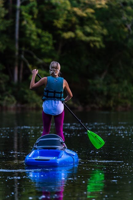 pexels photo 1504215 1504215 A woman enjoys stand-up kayaking on a calm lake surrounded by lush greenery, wearing a life vest.