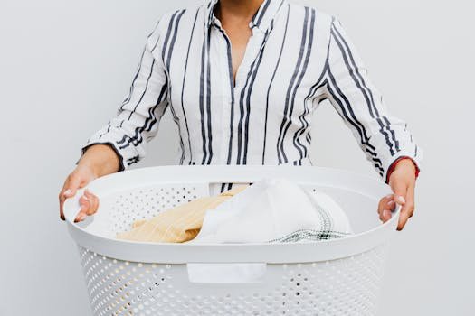 pexels photo 4959879 4959879 A woman holding a laundry basket filled with clothes against a plain white background.